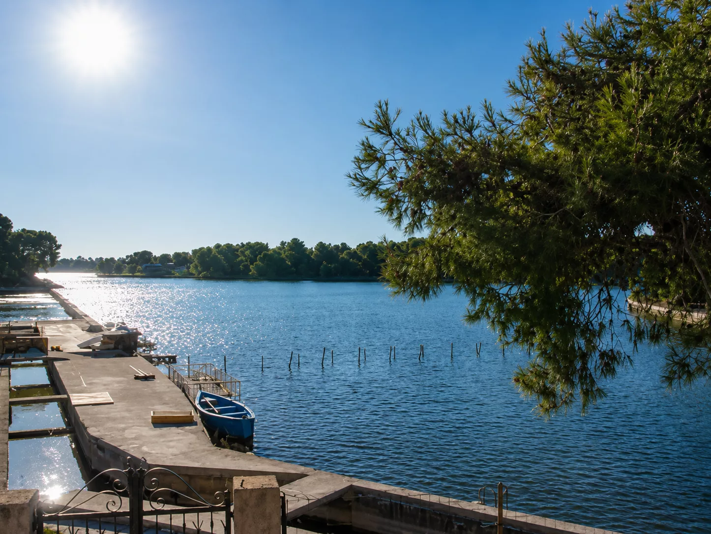 Veduta dei Laghi Alimini con il piccolo molo e una barca, immersi nella vegetazione mediterranea.