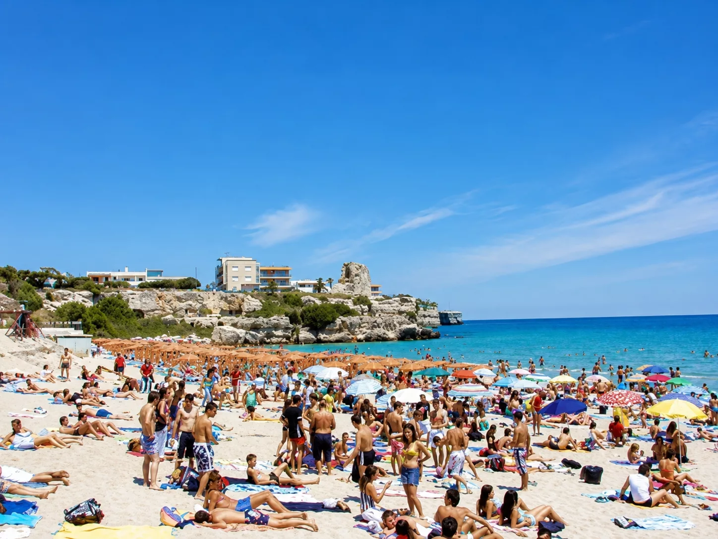 Spiaggia in piena estate di Torre dell’Orso, con sabbia chiara, mare azzurro e numerosi bagnanti durante una giornata estiva.